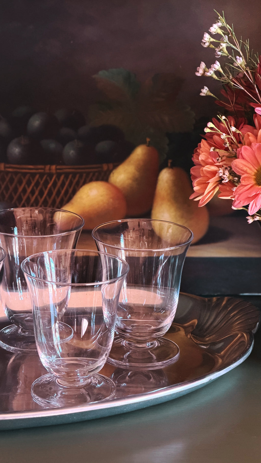 Vintage Crystal Cocktail & Juice Glasses arranged on a reflective silver tray, set against a dark rustic background with pears, flowers, and fruit.