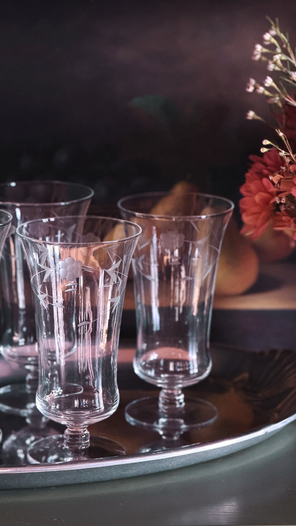 A Set of 4 Vintage Etched Floral Iced Tea Glasses  with etched floral patterns, arranged on a reflective silver tray against a dark, moody background with dried flowers.