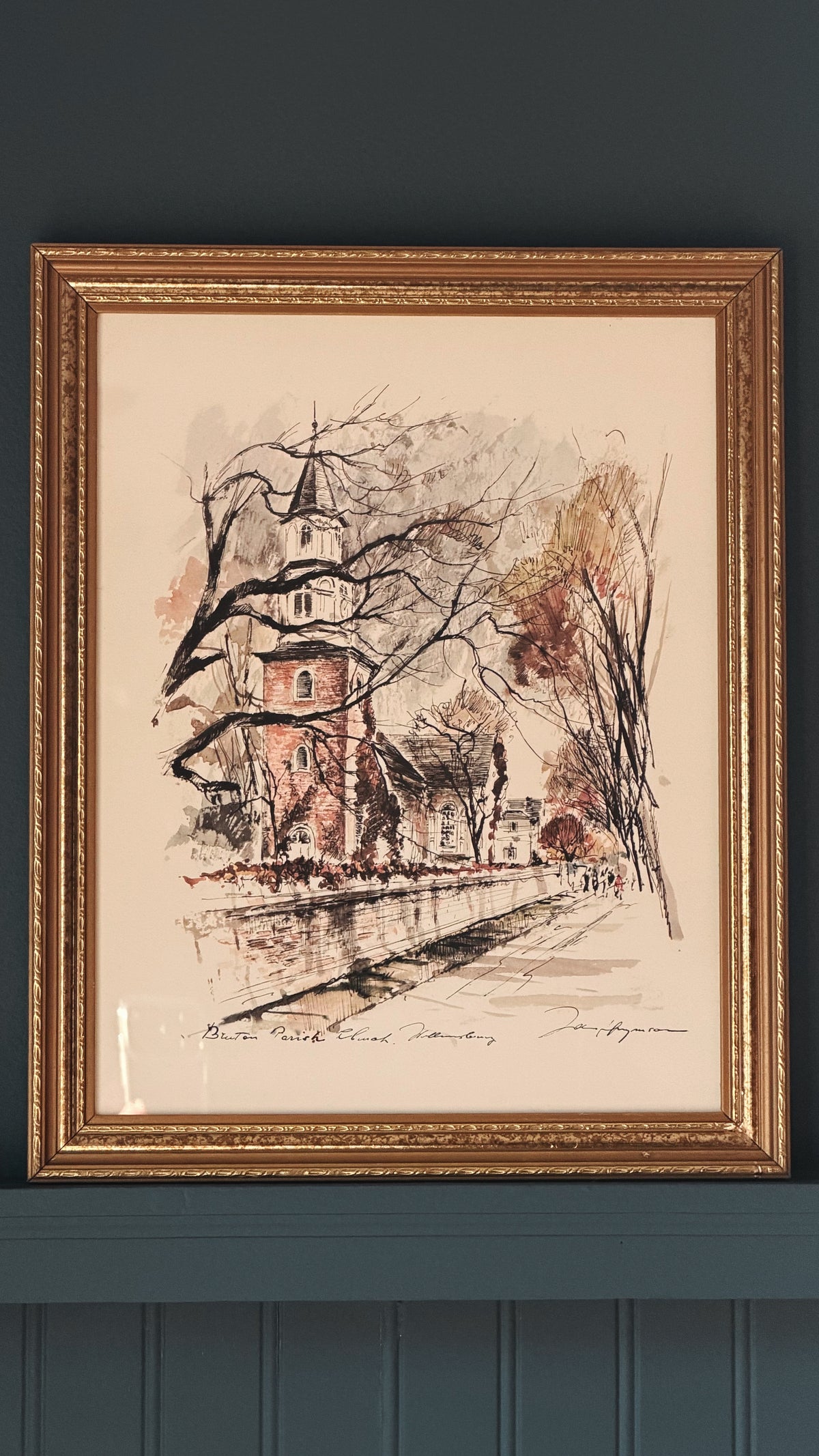 Vintage John Haymson Bruton Parish Church Williamsburg Framed Print. A framed art print depicting a sketch of a church and street scene, mounted on a dark teal wall.
