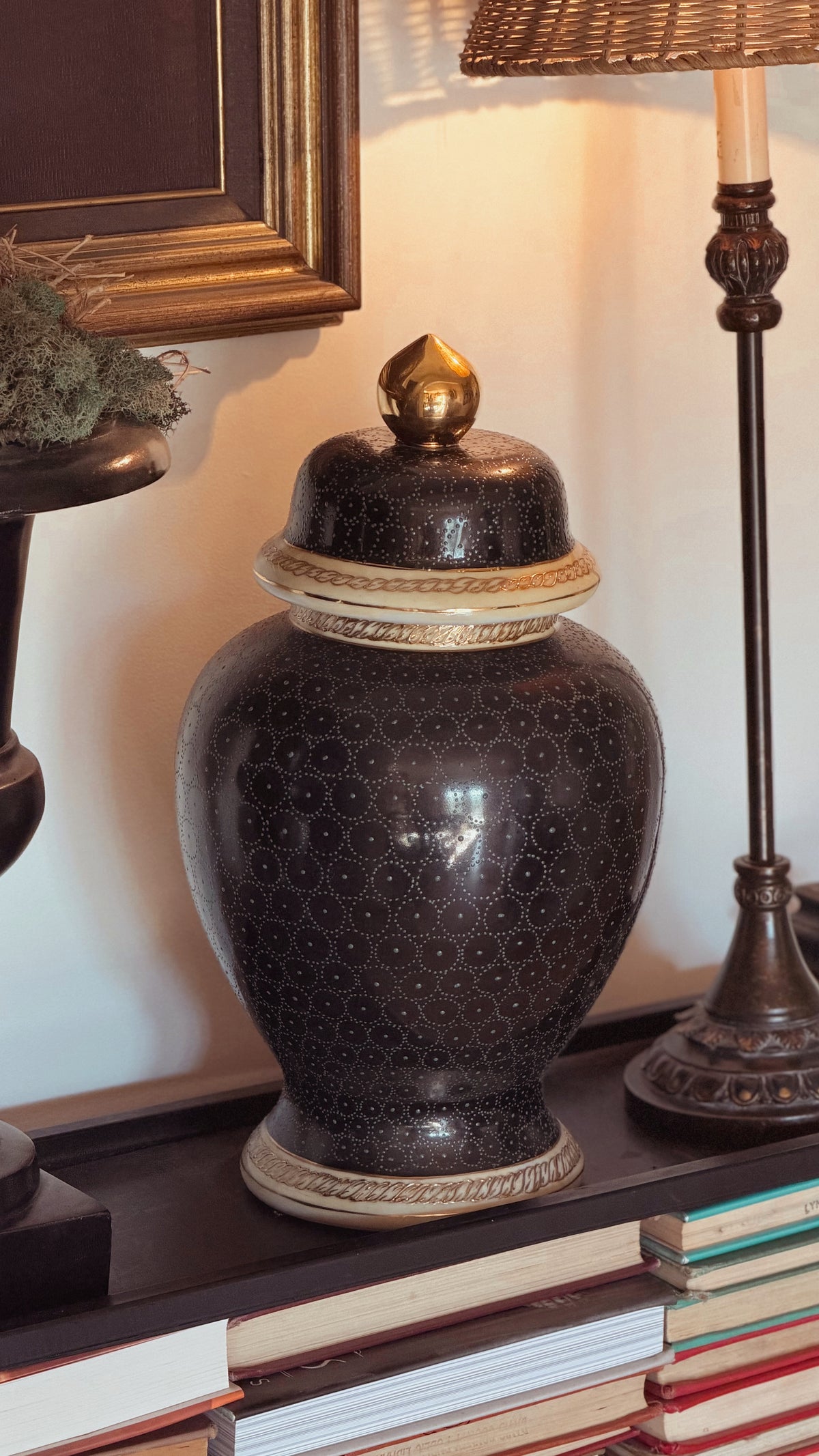 Large Hand Painted Lidded Jar with a textured pattern and gold-toned accents, displayed on a shelf next to a lamp and books.