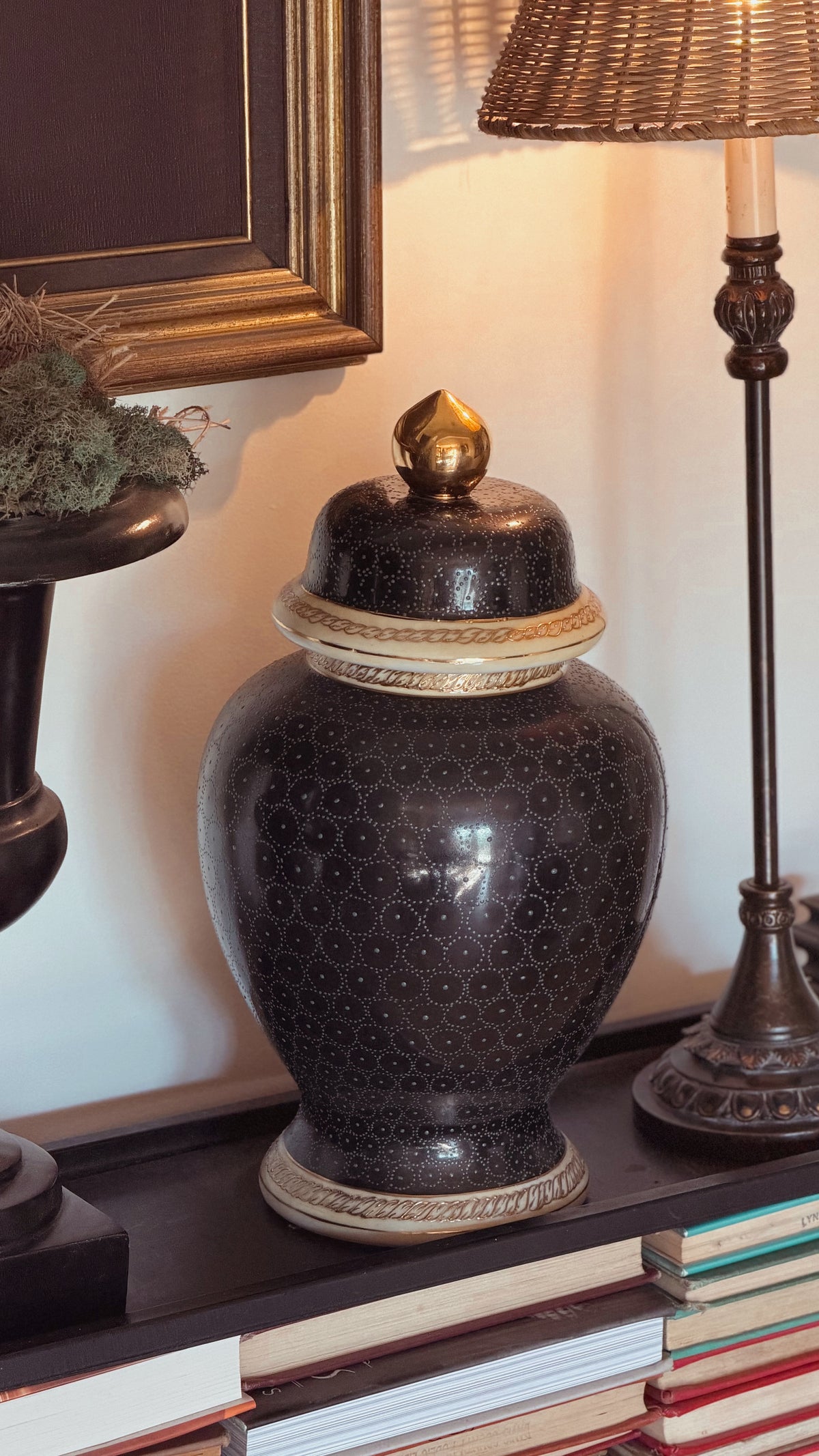A Vintage Navy Blue Ginger Jar with a gold-toned finial and cream decorative bands, displayed on a shelf next to a lamp and books.