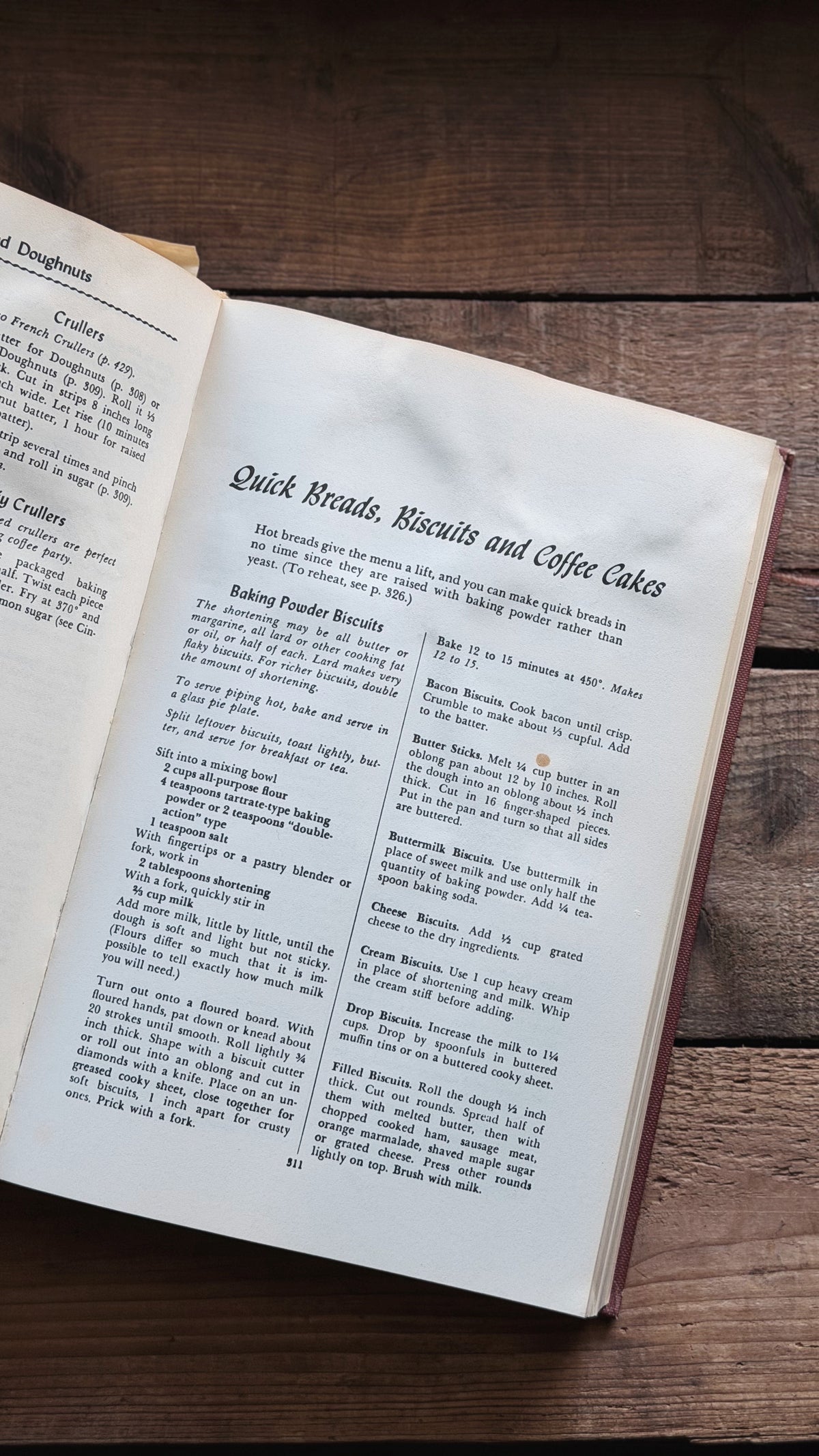 An open vintage cookbook spread on a dark wooden table, showing printed recipe text for quick breads, biscuits, and coffee cakes.