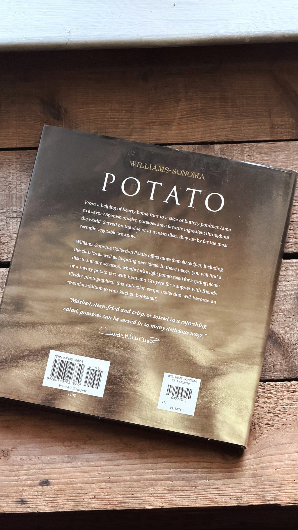 The back cover of the book 'Potato' by Williams-Sonoma, featuring a textured metallic gold and bronze background with white text, resting on a rustic wooden surface.