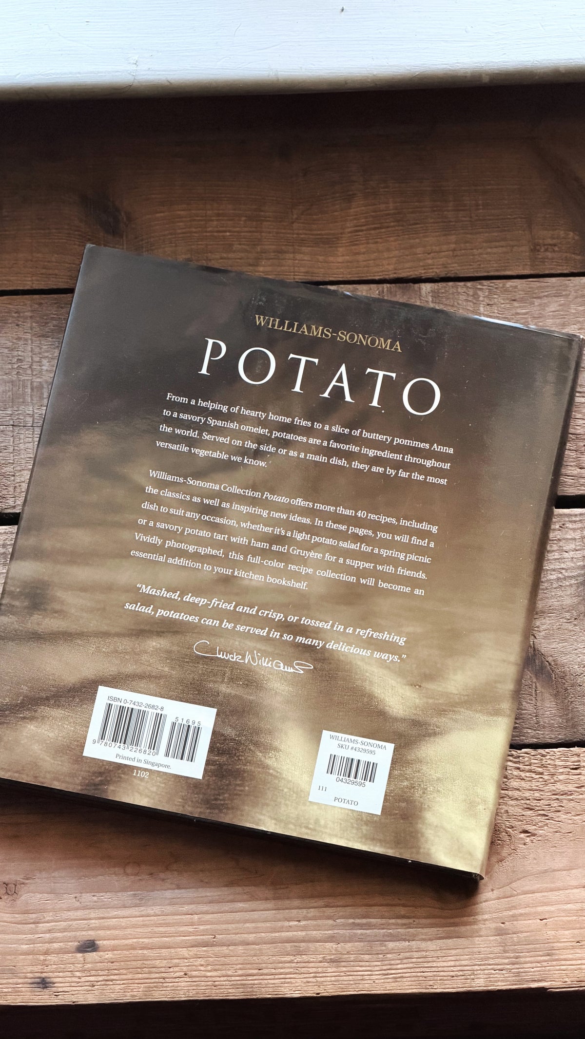The back cover of the book 'Potato' by Williams-Sonoma, featuring a textured metallic gold and bronze background with white text, resting on a rustic wooden surface.