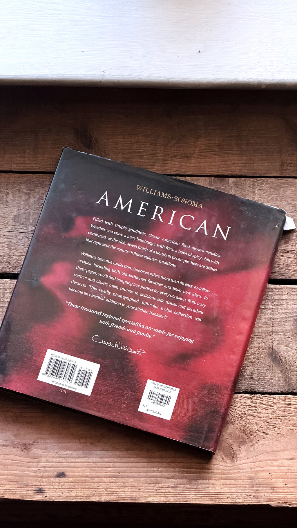 The back cover of the book 'American' by Williams-Sonoma, featuring a red and black abstract design, resting on a rustic wooden surface.