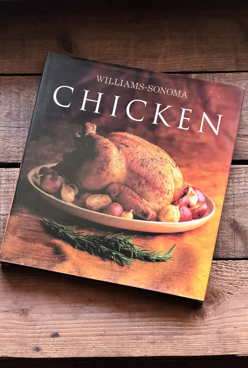 Williams-Sonoma Chicken cookbook resting on a rustic wooden surface, showing a roasted chicken cover photo on the front.