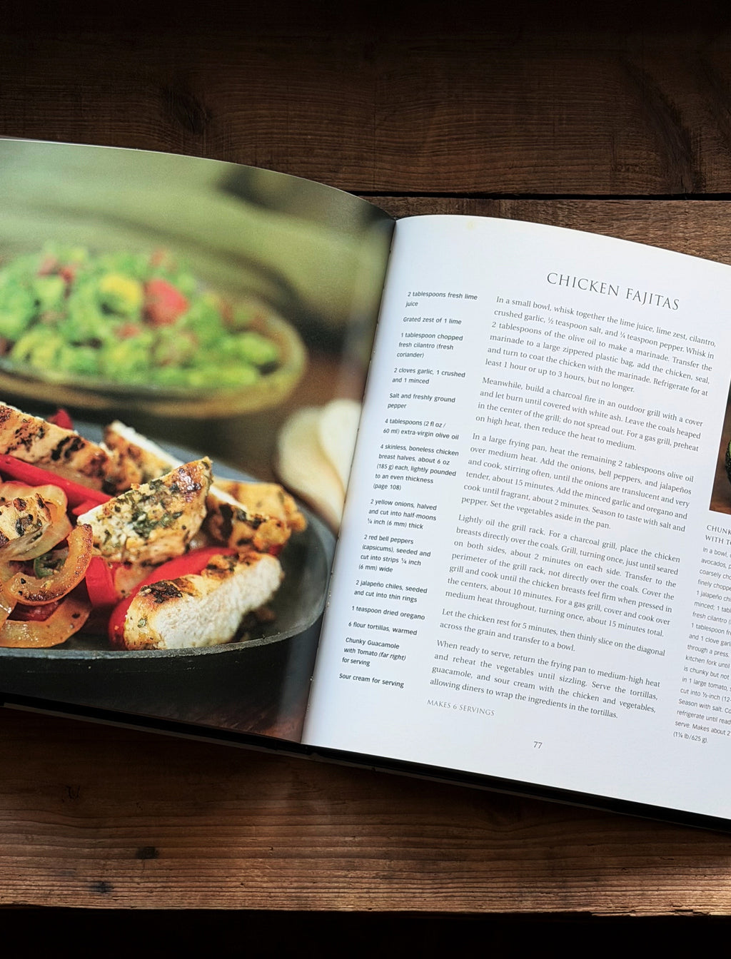 An open hardcover cookbook lying on a dark wooden table, showing a large food photograph of grilled chicken fajitas on the left page and the recipe title 'CHICKEN FAJITAS' with columns of text on the right page.