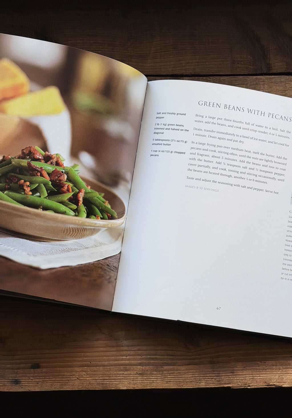 An open cookbook lying on a dark wooden table, showing a recipe page for green beans with pancetta. The left page features a color photograph of the prepared dish, while the right page contains the recipe text.