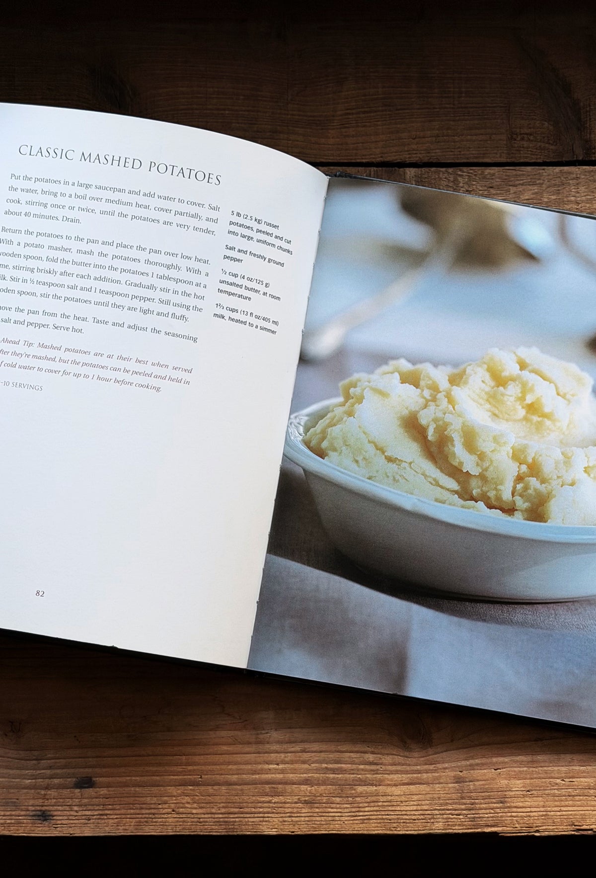 An open cookbook spread on a wooden table, showing the recipe for Classic Mashed Potatoes on the left page and a photo of mashed potatoes in a bowl on the right page.