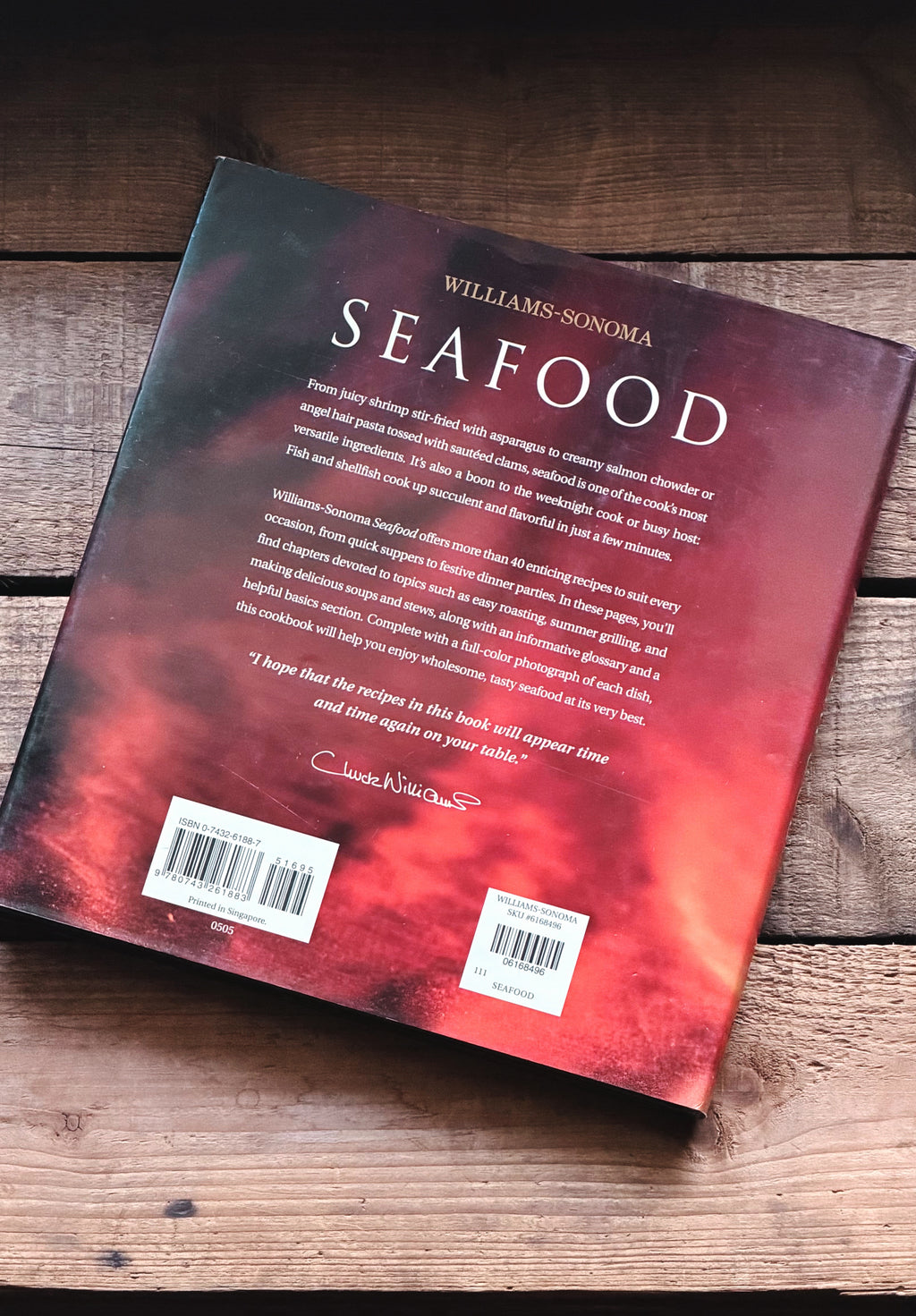 The back cover of the book 'Seafood' by Williams-Sonoma, featuring a red and black abstract design, photographed on a rustic wooden surface.