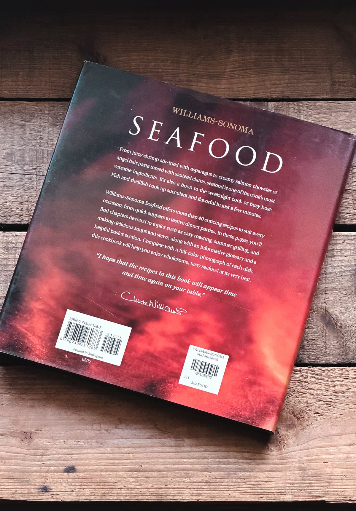 The back cover of the book 'Seafood' by Williams-Sonoma, featuring a red and black abstract design, photographed on a rustic wooden surface.