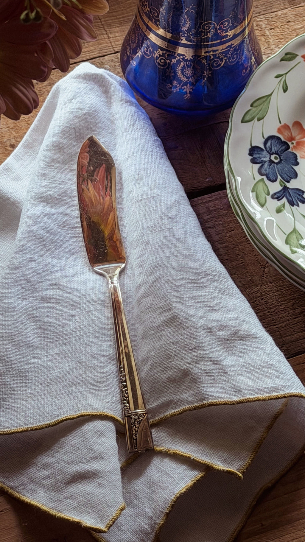 A decorative butter knife with an ornate  handle, resting on a folded white linen napkin on a wooden table.