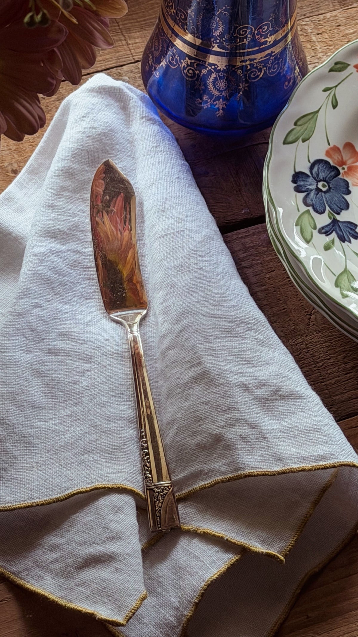 A decorative butter knife with an ornate  handle, resting on a folded white linen napkin on a wooden table.