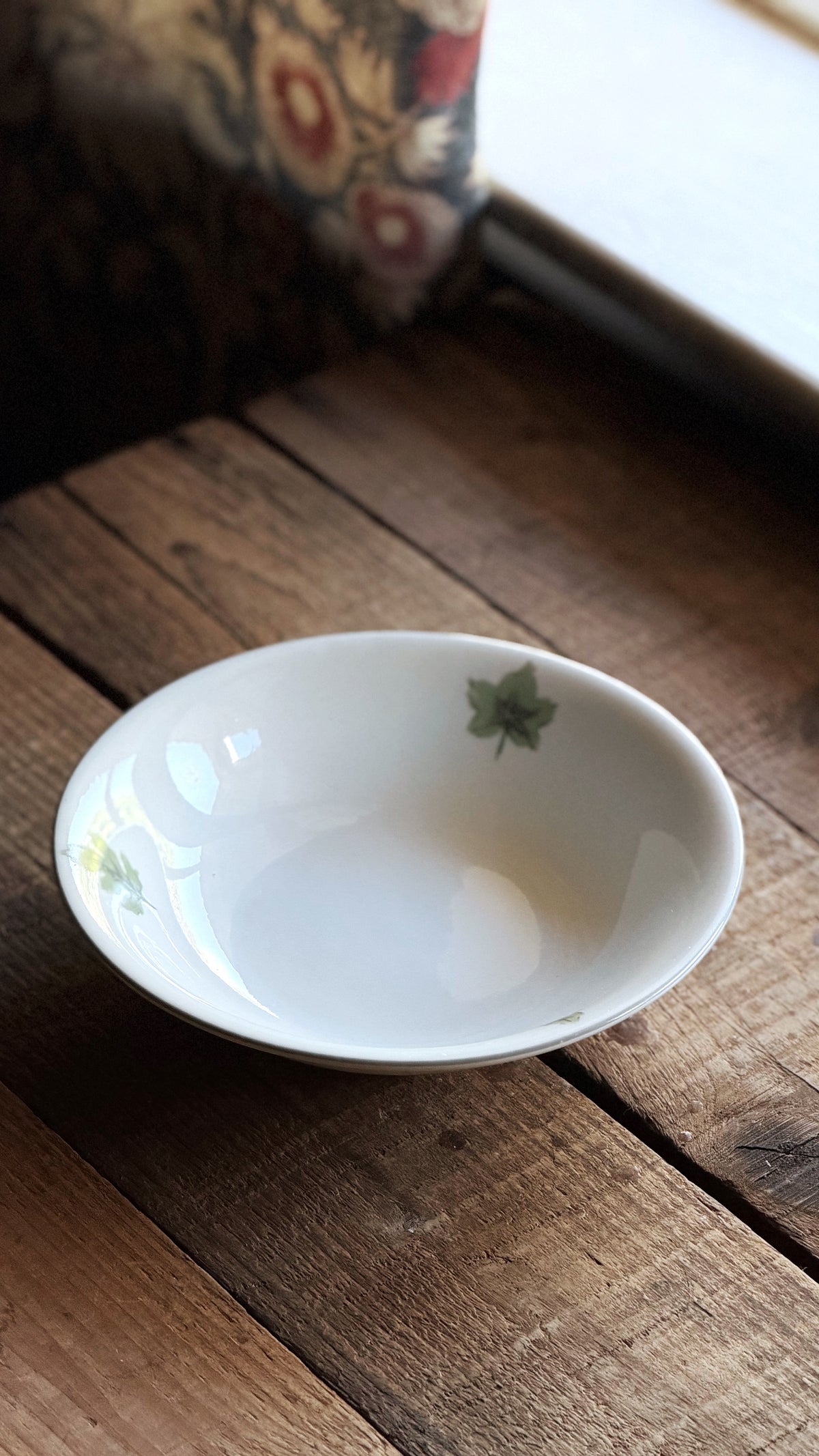 A small white stoneware bowl with delicate green floral illustrations, resting on a rustic wooden surface.
