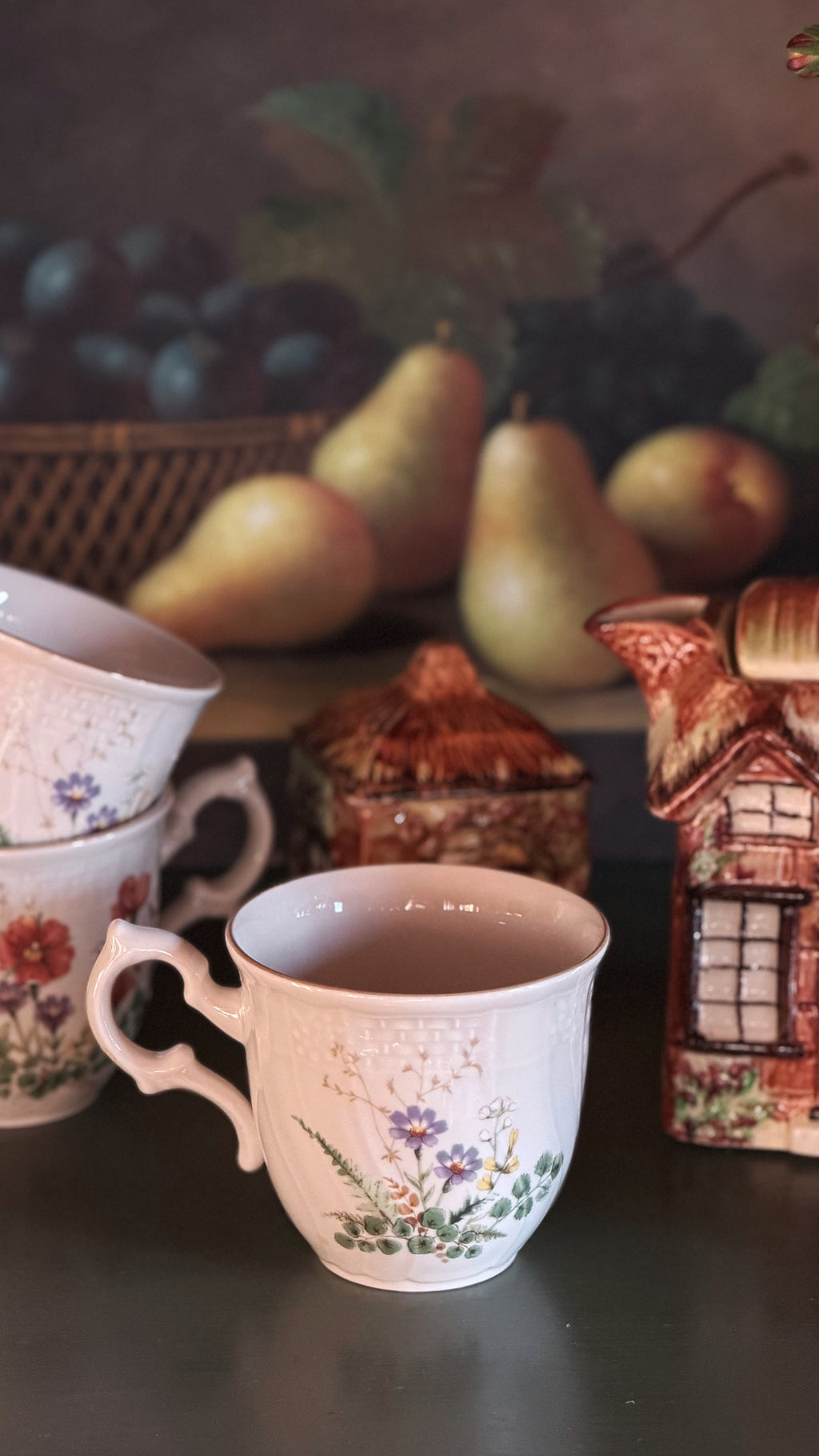 A set of Mikasa Margaux Flat Cups arranged on a dark tabletop with decorative props including pears and a small house figurine.
