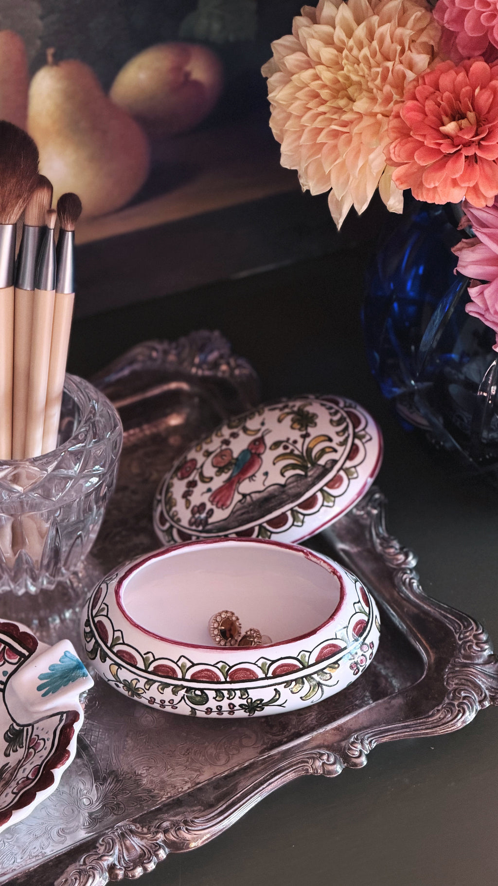 A decorative oval jewelry box with a removable lid, shown open on an ornate silver tray. The box has a white base with intricate red, green, and gold floral and bird motifs.