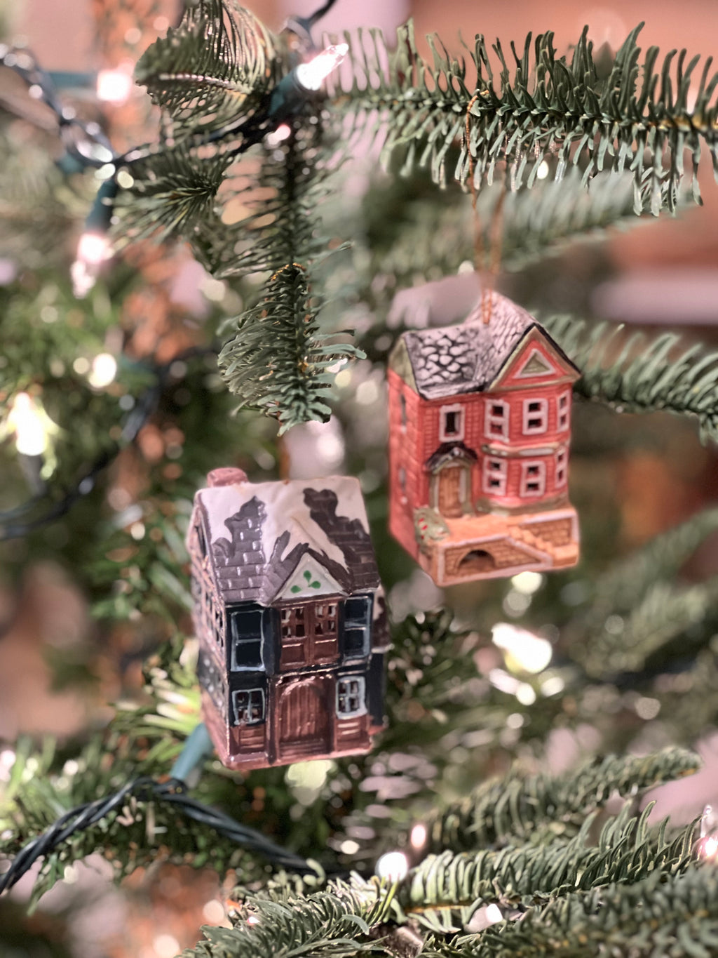 Two small house-shaped Christmas ornaments hanging on a decorated tree.