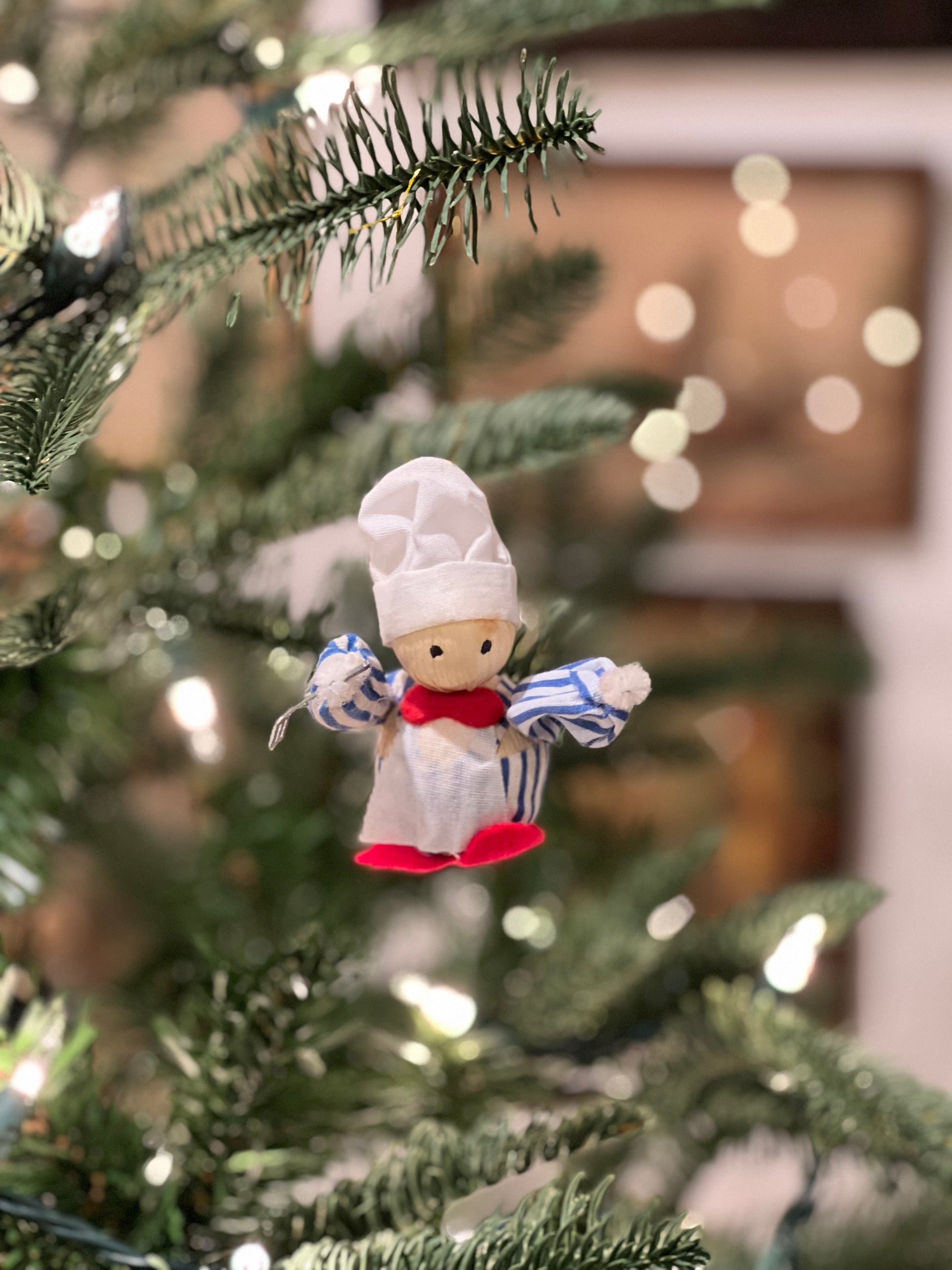 Decorative chef figurine on a Christmas tree with blurred lights in the background