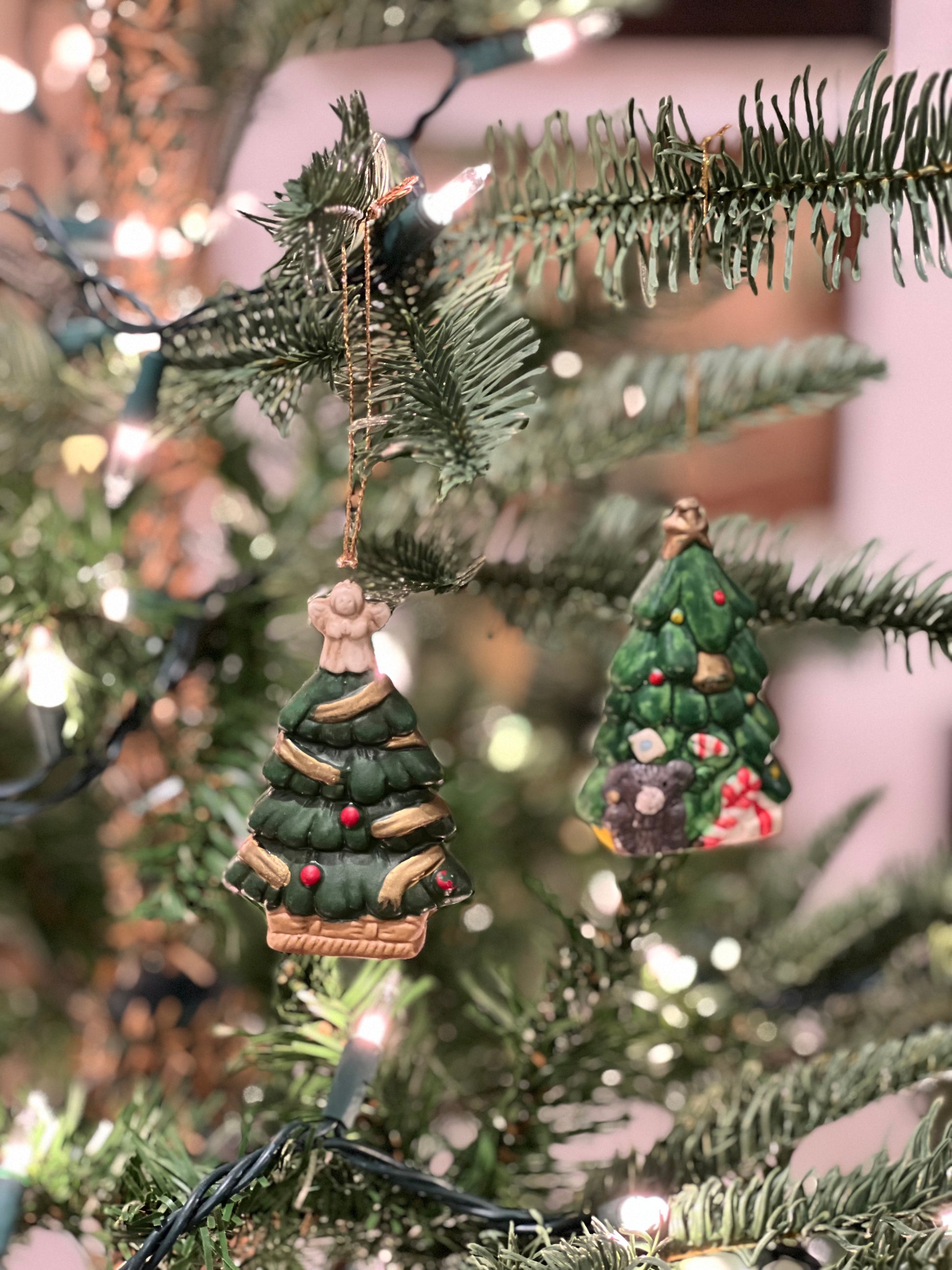 Two Christmas tree ornaments on a decorated tree with lights.