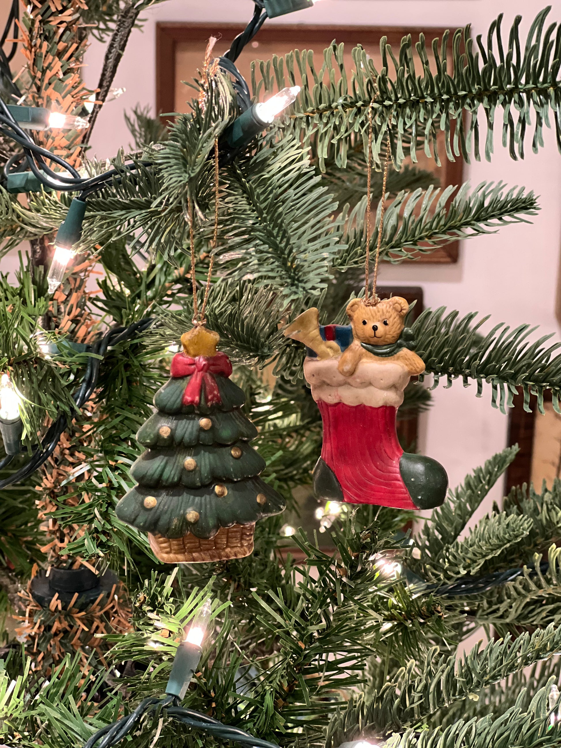 Decorative Christmas ornament of a teddy bear and green tree on a lit Christmas tree.
