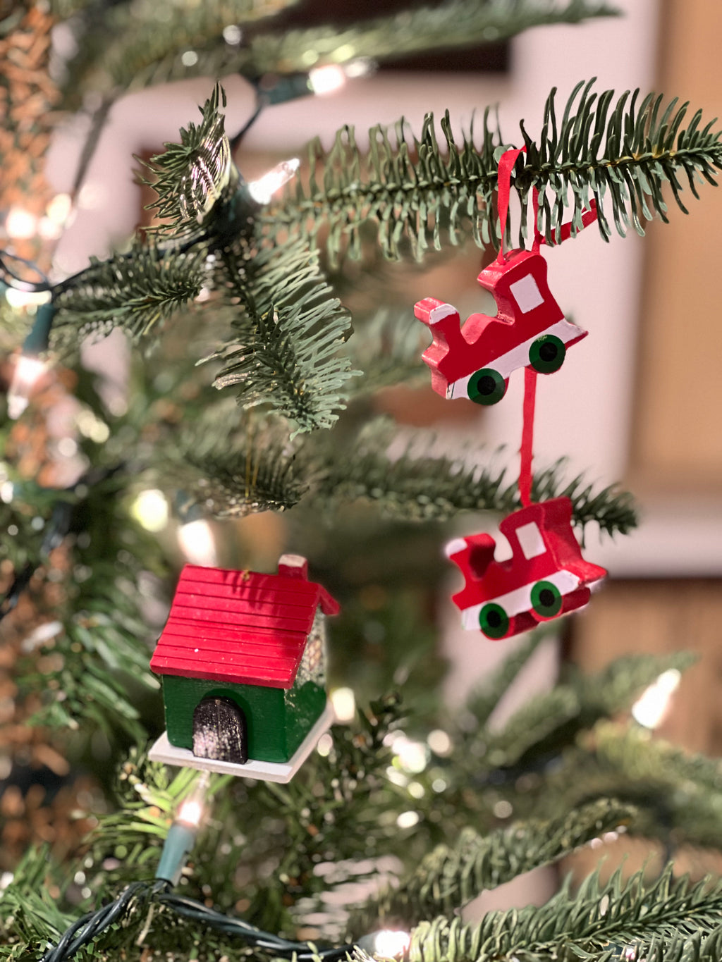 Decorative Christmas ornaments on a tree, including a red house and a red sleigh.