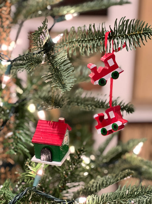 Decorative Christmas ornaments on a tree, including a red house and a red sleigh.