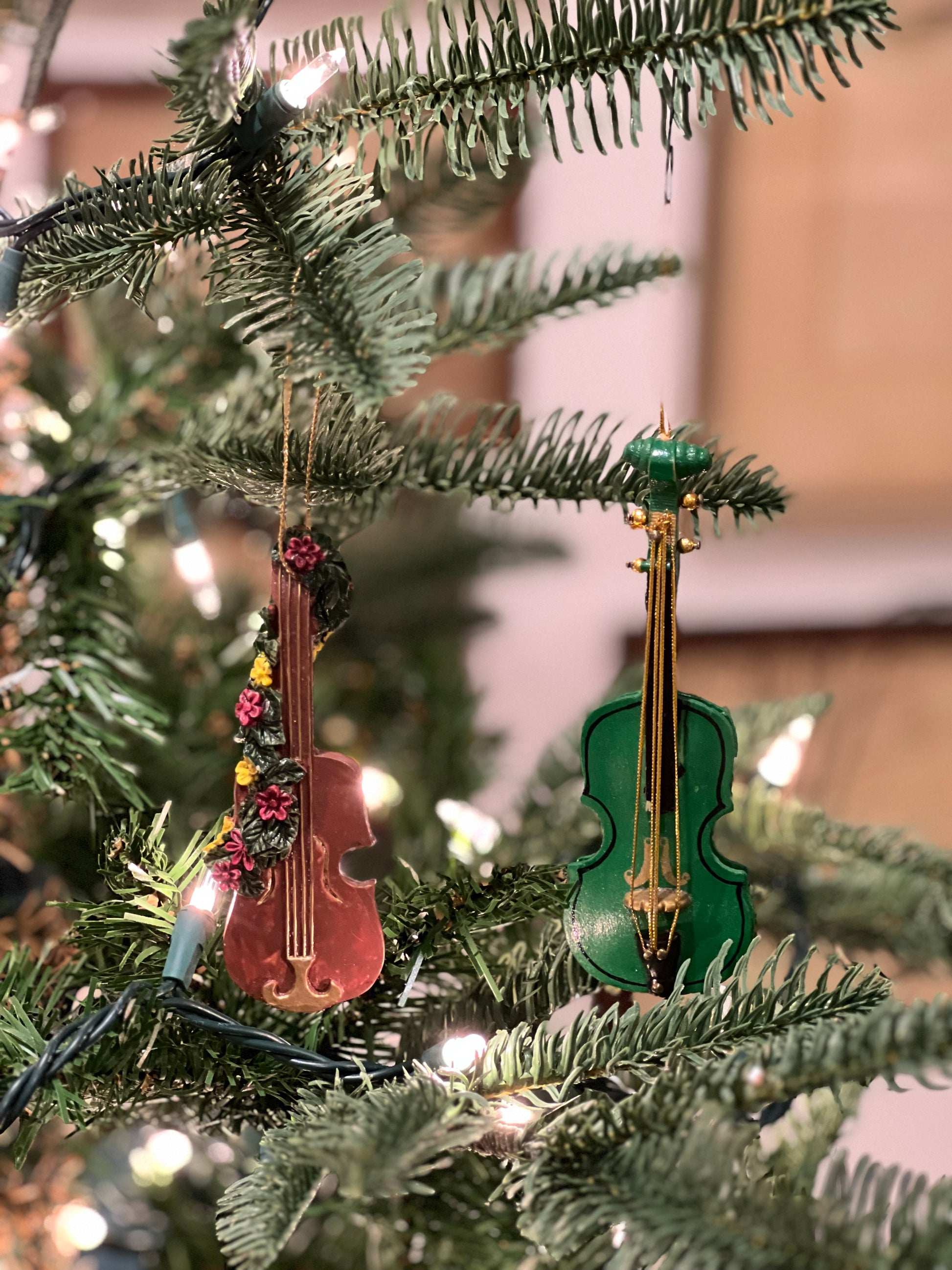Two violin-shaped Christmas tree ornaments on a decorated tree.