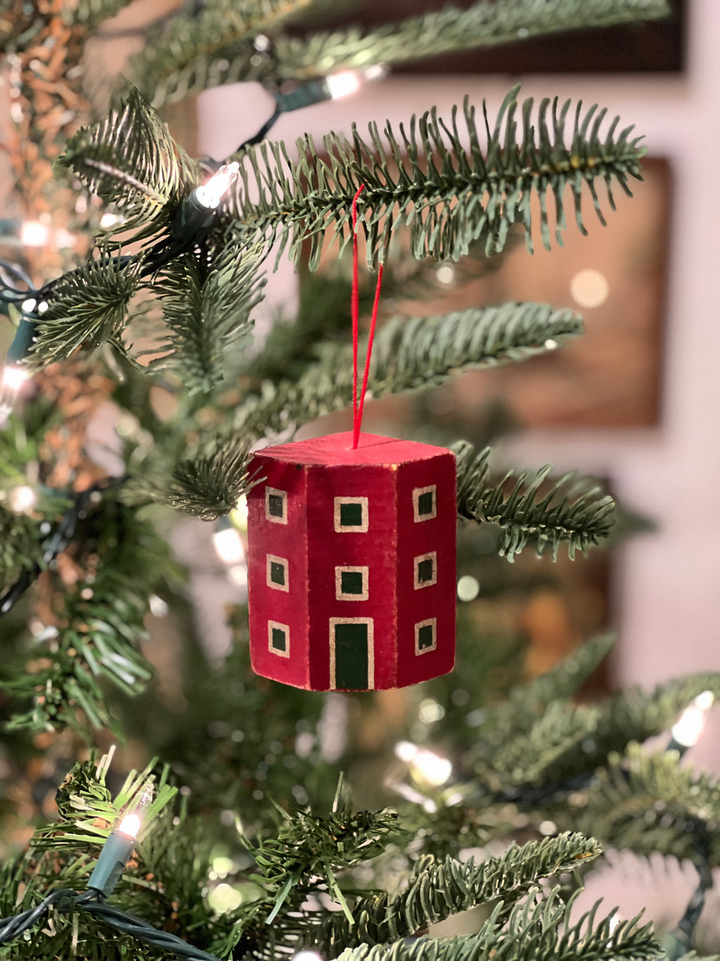 Red house-shaped ornament on a Christmas tree with blurred lights in the background