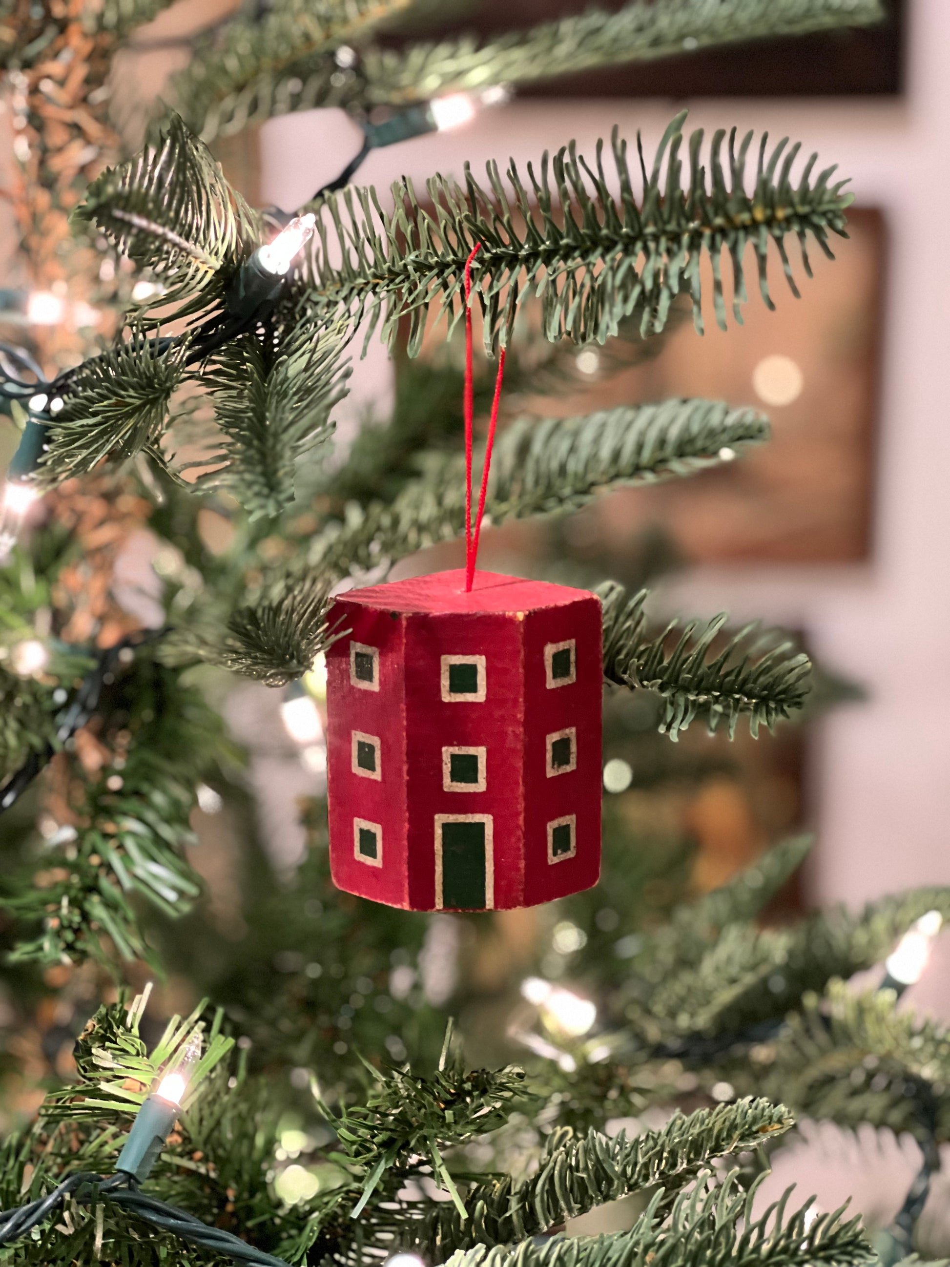 Red house-shaped ornament on a Christmas tree with blurred lights in the background