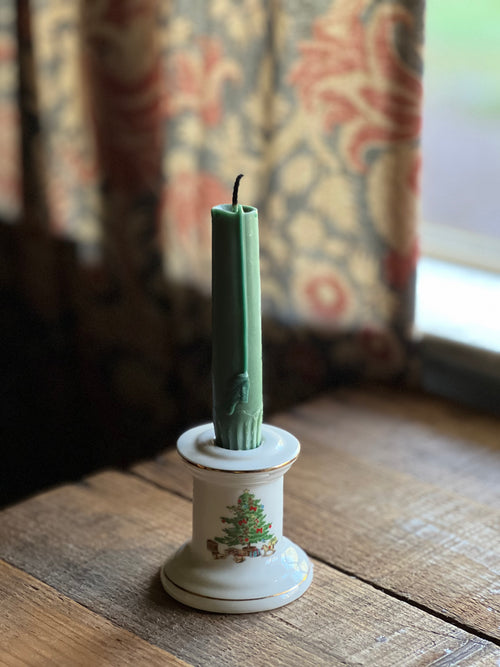 Green candle in a decorative holder on a wooden surface with floral curtains in the background
