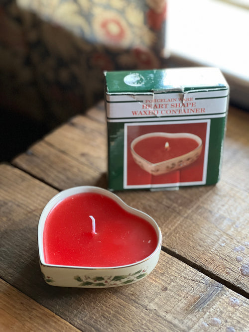 Heart-shaped red candle with a box in the background on a wooden surface