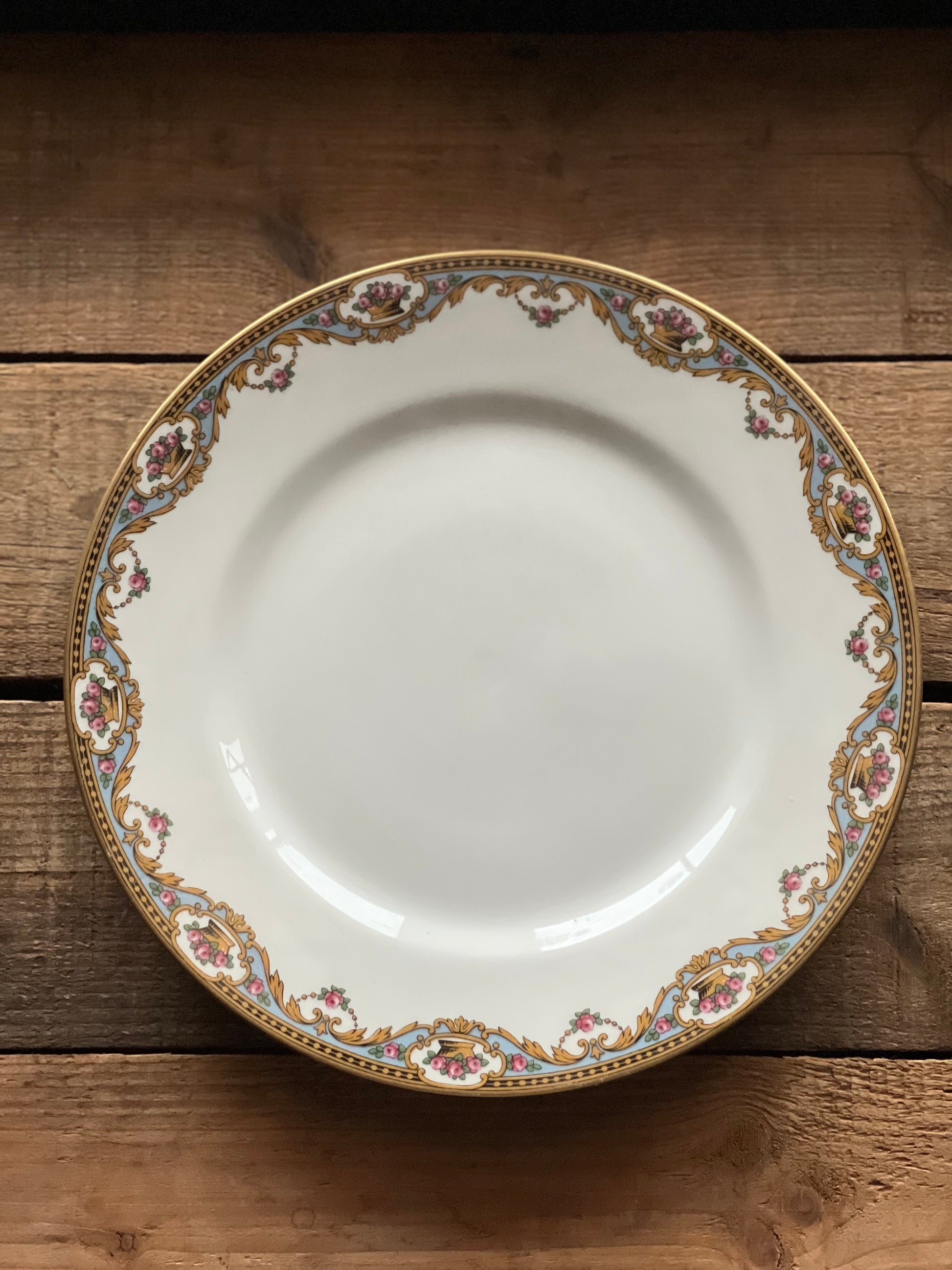 White ceramic plate with decorative gold and floral rim on a wooden surface