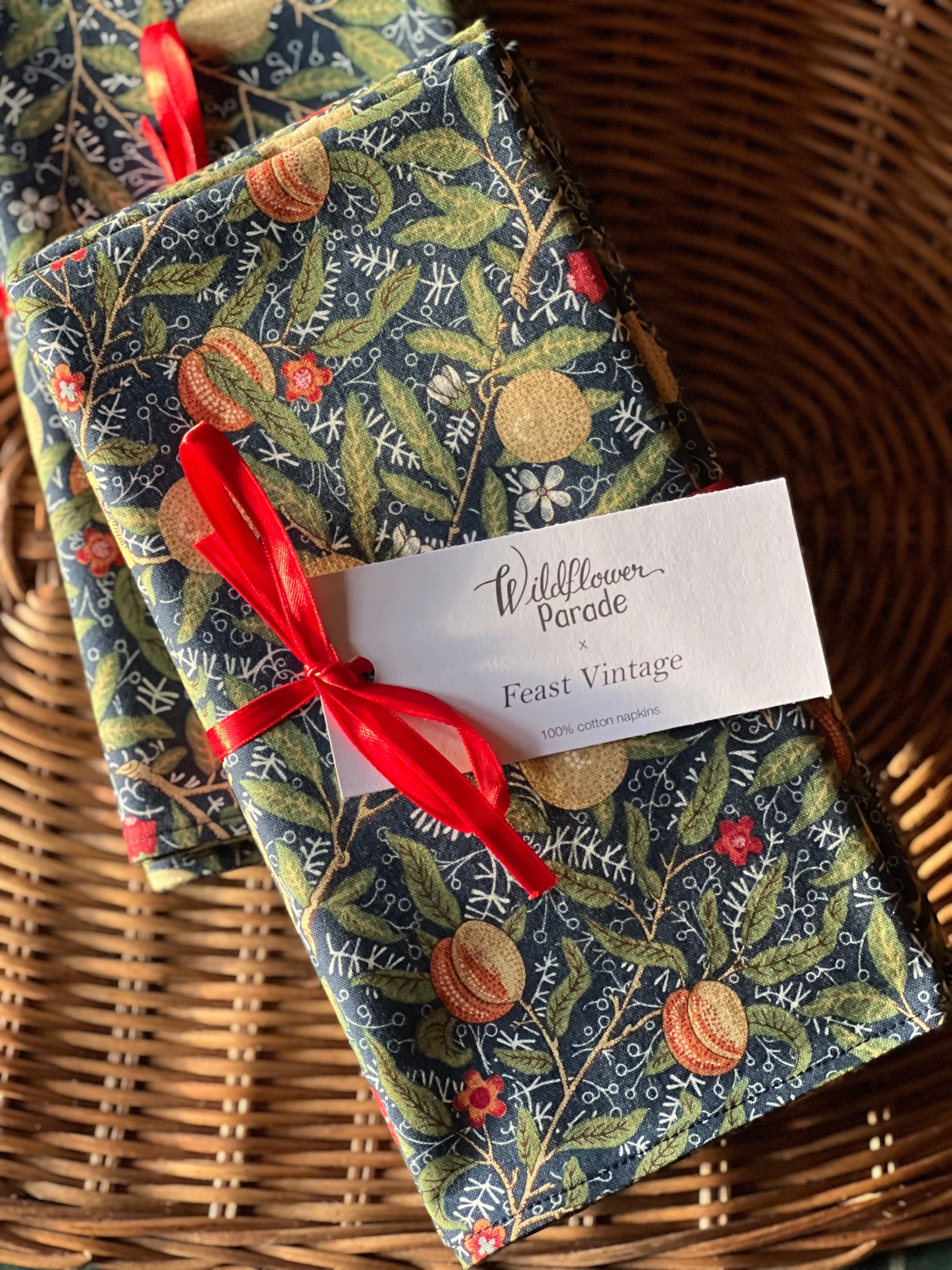 Two patterned napkins tied with a red ribbon on a woven surface, with a card labeled 'Wildflower Parade Feast Vintage'.