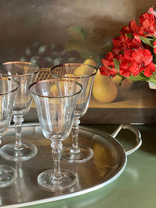 Set of clear glass goblets on a silver tray with red flowers and pears in the background.