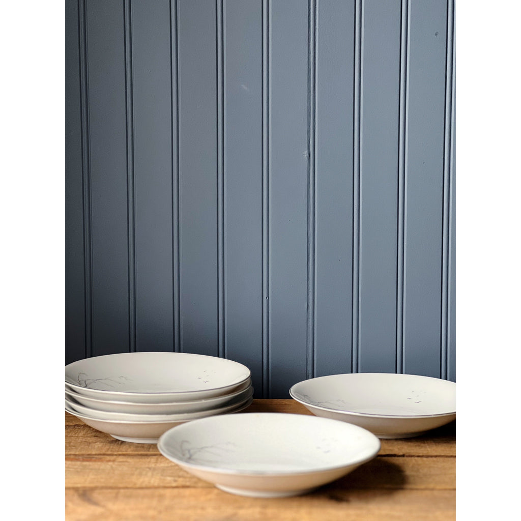 Set of white Winterling bowls on a wooden surface with a blue paneled wall in the background