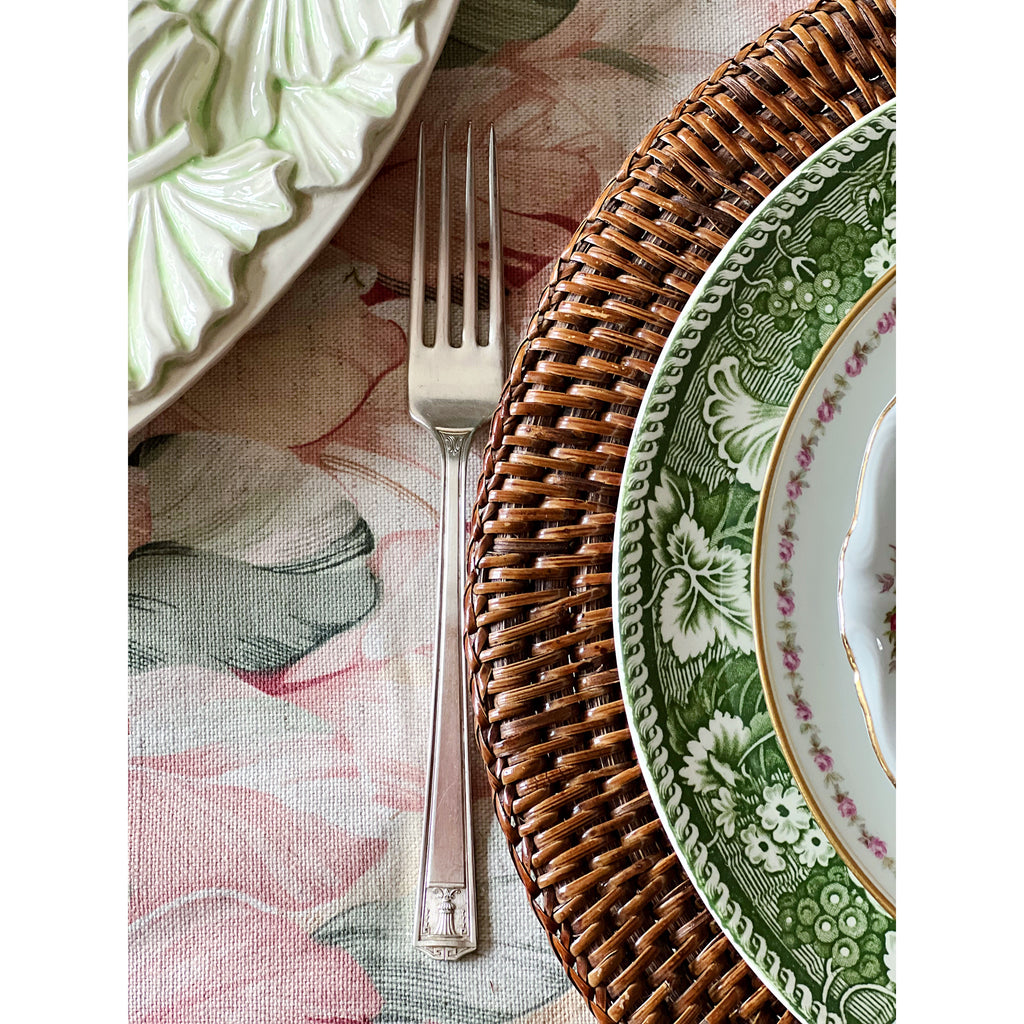 Dining setting with floral plates, wicker charger, and silver fork on a patterned tablecloth.