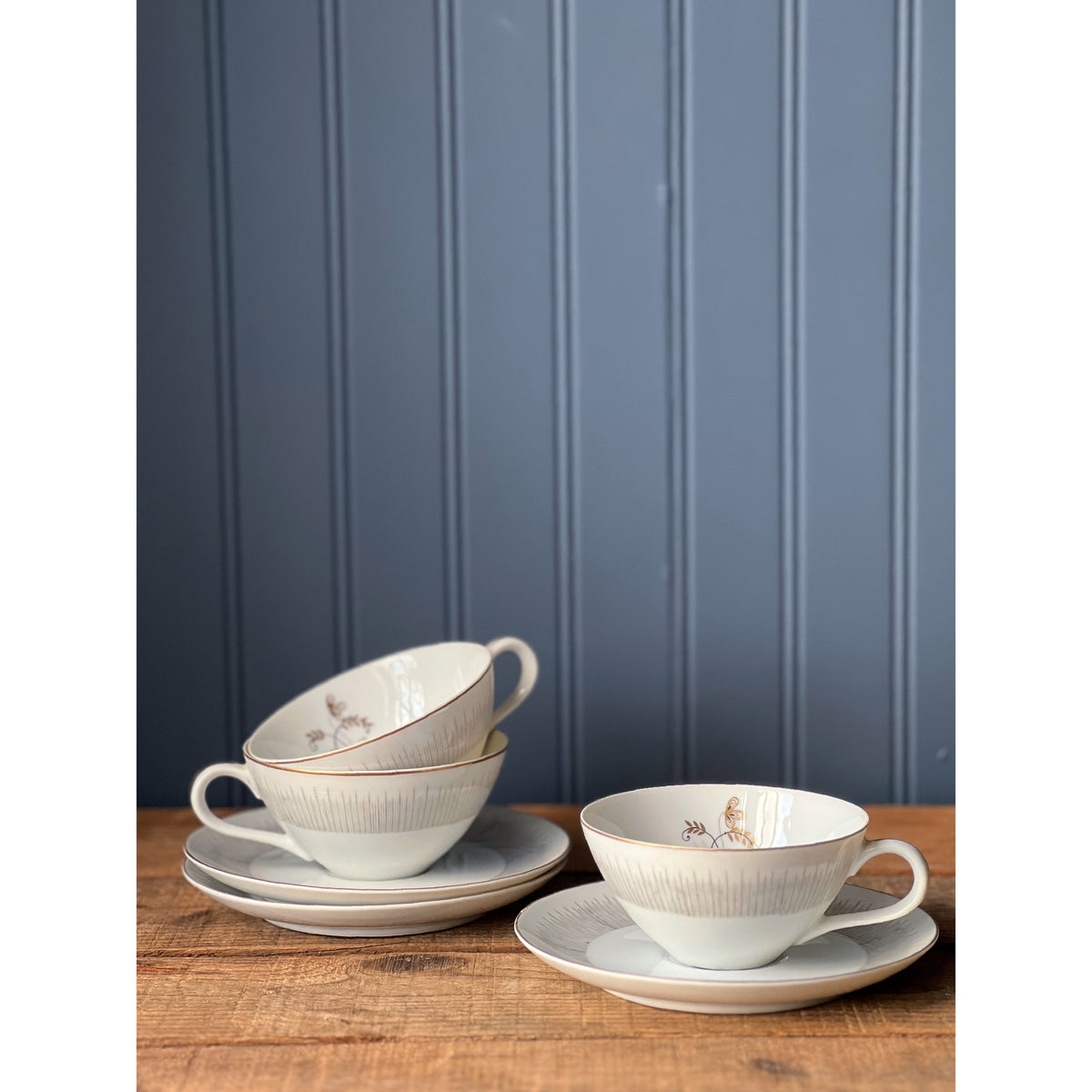 Set of tea cups and saucers on a wooden table with a blue paneled wall background