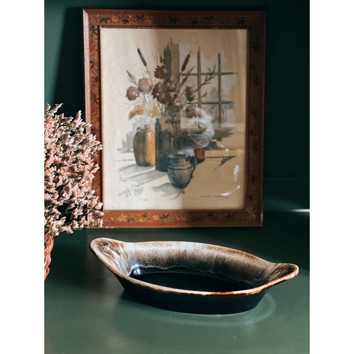Vintage Pfaltzgraff Gourmet Brown Au Gratin Dish on a dark surface with a framed painting of flowers in the background.