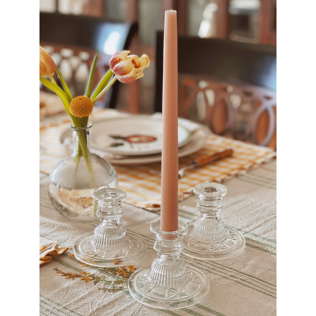 Pink candle in a glass holder on a table with flowers and plates