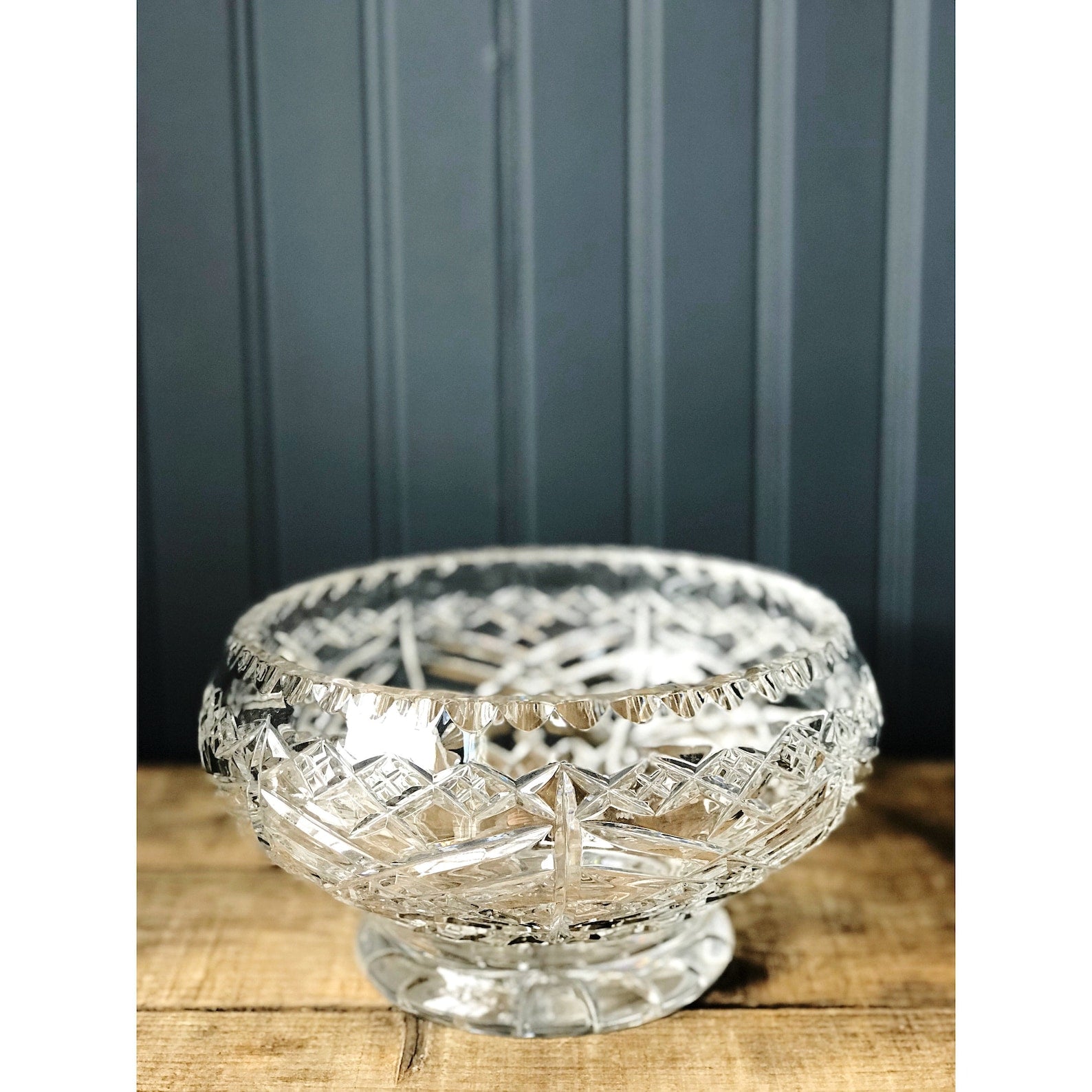 A clear, vintage footed crystal serving bowl with a starburst footed design and X pattern around the exterior, displayed against a grey background.