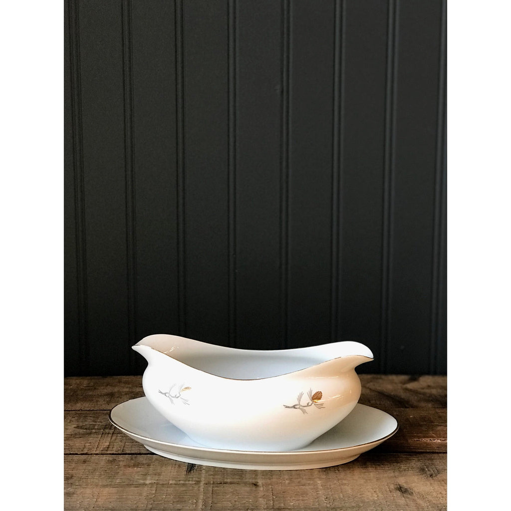 White gravy boat with pinecone design on a wooden surface against a blue paneled wall