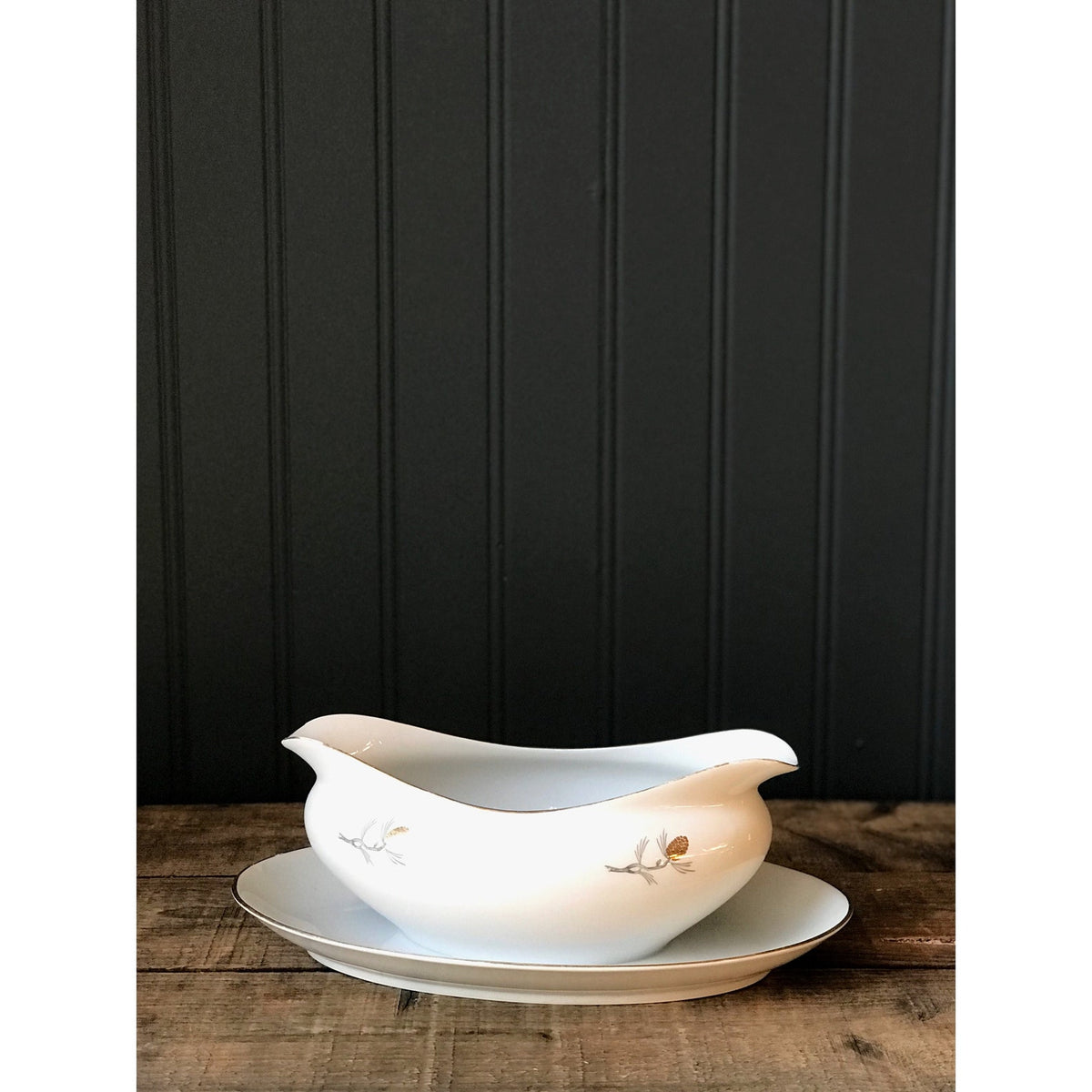 White gravy boat with pinecone design on a wooden surface against a blue paneled wall