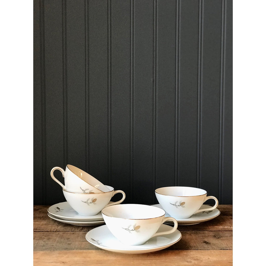 Set of ceramic tea cups and saucers on a wooden surface with a black paneled wall background.